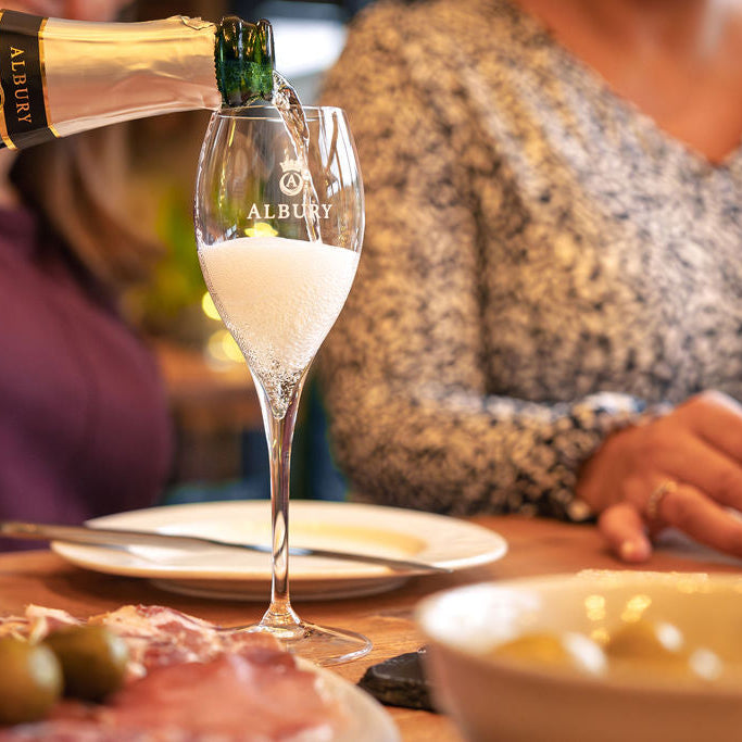 Albury champagne being poured into a glass with a person sitting at a table in the background.