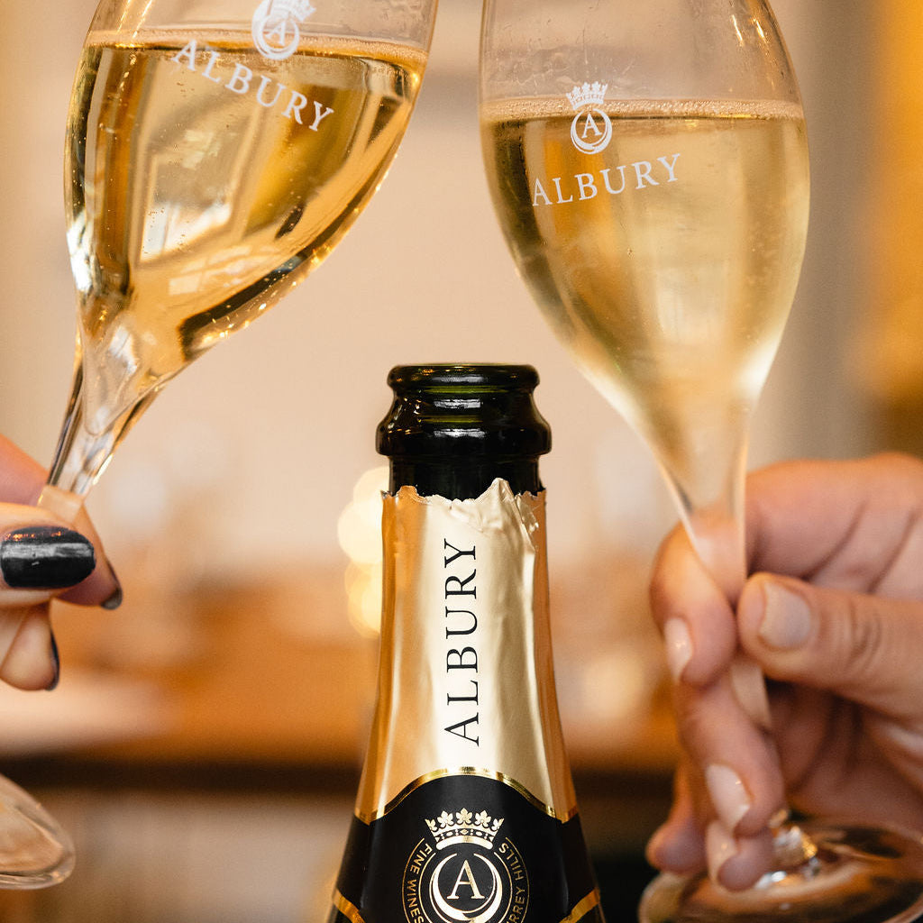 Two glasses of Albury champagne being held up with a bottle in the foreground.