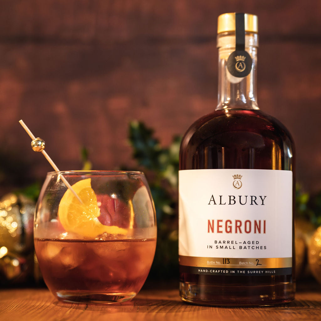 Albury Negroni bottle with a cocktail garnished with an orange slice on a wooden surface.