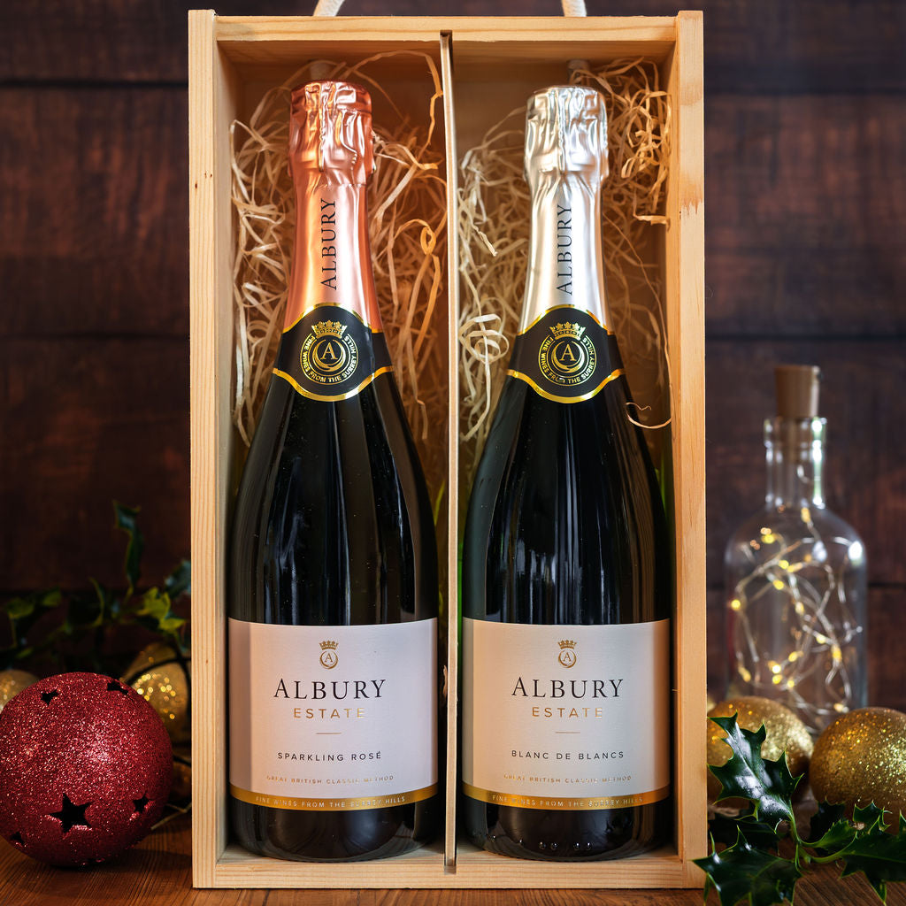 A wooden gift box containing two Albury Estate sparkling wines, one Rosé and one Blanc de Blancs, styled with holiday decorations on a dark wooden table.