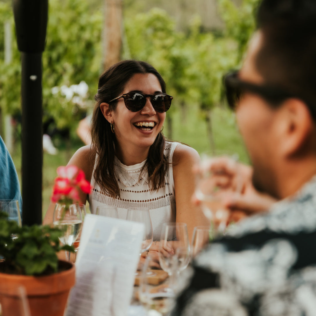 Woman in sunglasses laughing with a man at an outdoor dining table.